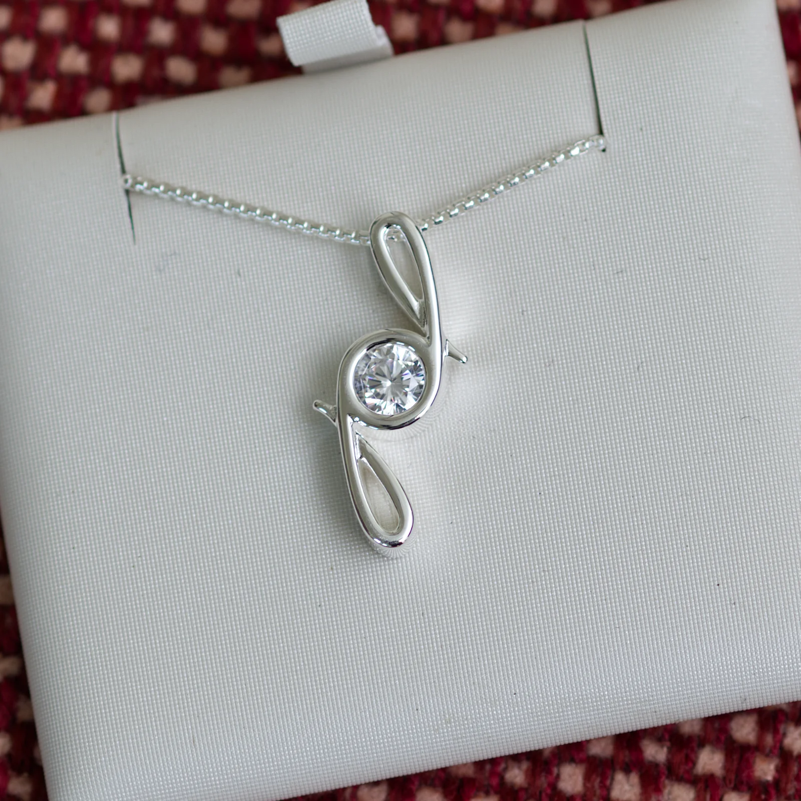 This pendant is made from tarnish resistant silver and features a simulated diamond birth stone. It hangs from a 1mm rounded box chain. The design is a signature motif that symbolizes our message that every life is a precious life.