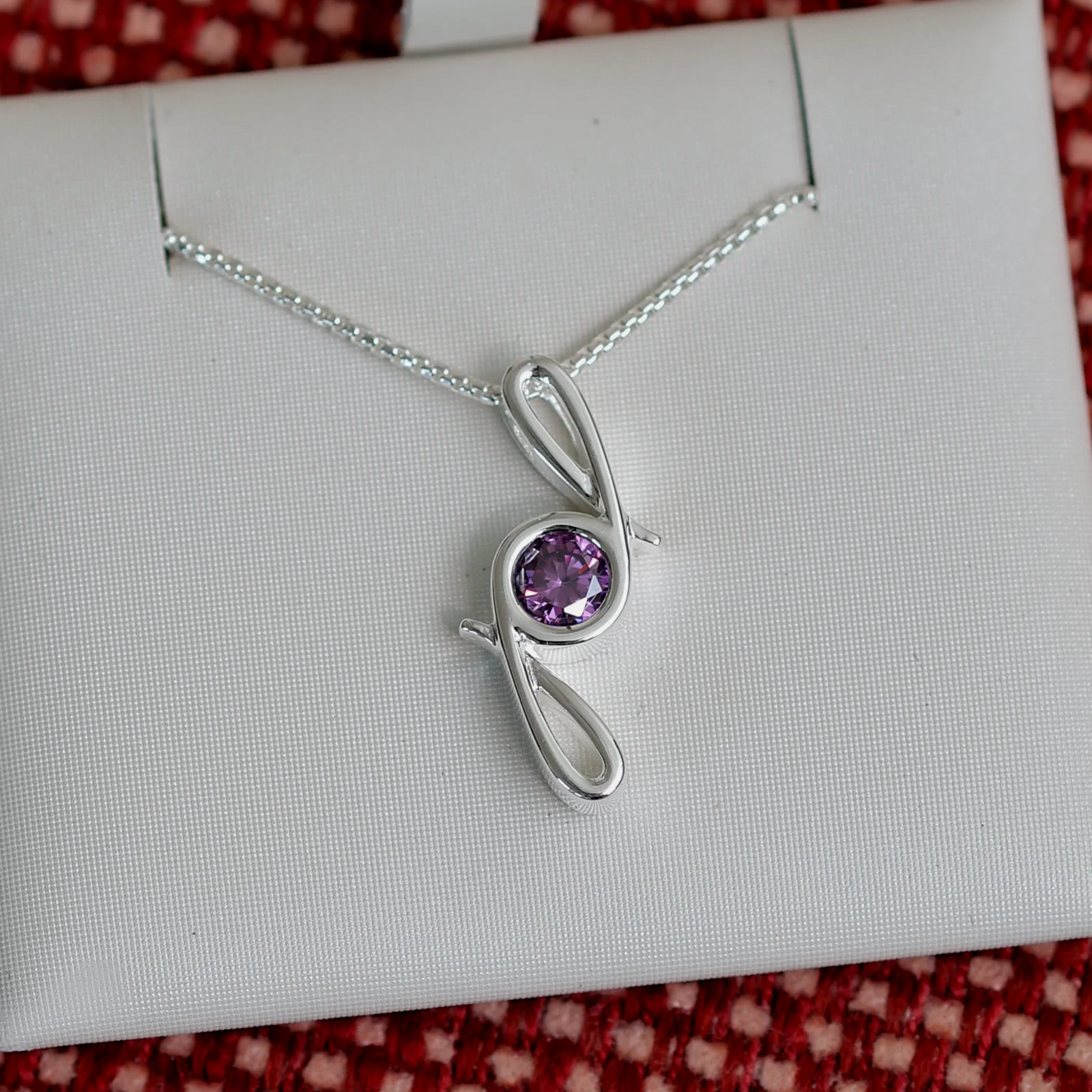 This pendant is made from tarnish resistant silver and features a simulated amethyst birth stone. It hangs from a 1mm rounded box chain. The design is a signature motif that symbolizes our message that every life is a precious life.