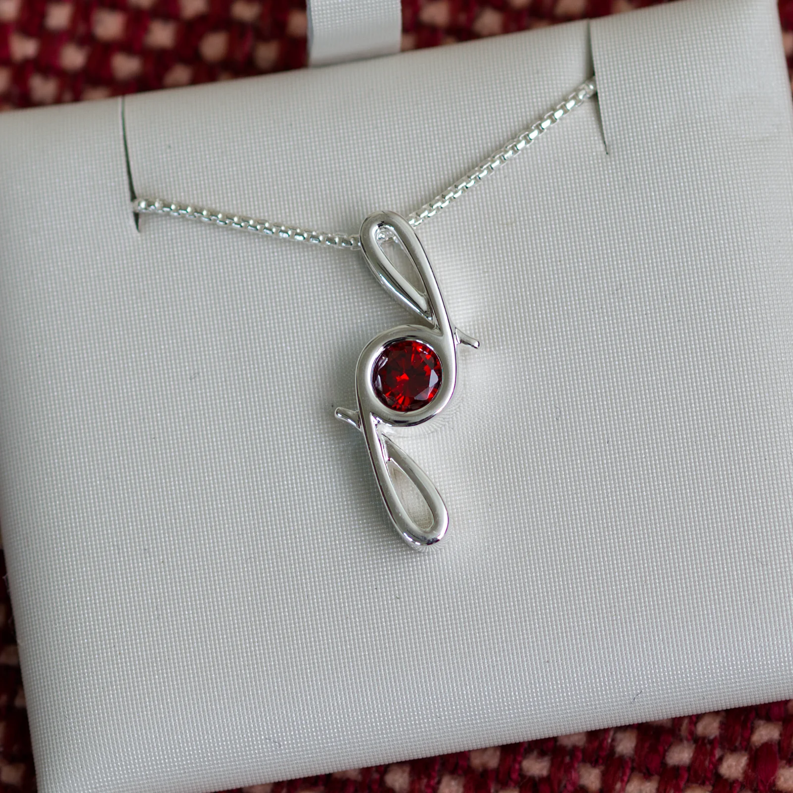 This pendant is made from tarnish resistant silver and features a simulated garnet birth stone. It hangs from a 1mm rounded box chain. The design is a signature motif that symbolizes our message that every life is a precious life.