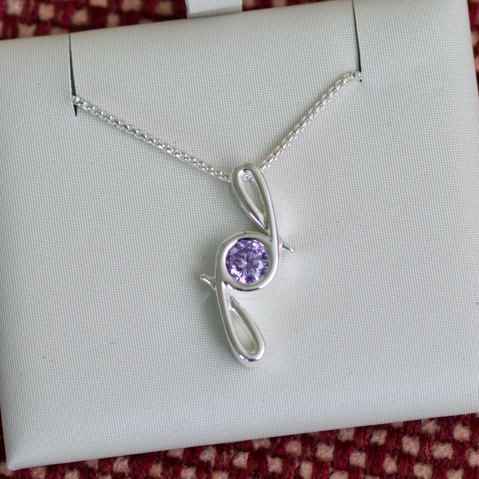 This pendant is made from tarnish resistant silver and features a simulated alexandrite birth stone. It hangs from a 1mm rounded box chain. The design is a signature motif that symbolizes our message that every life is a precious life.