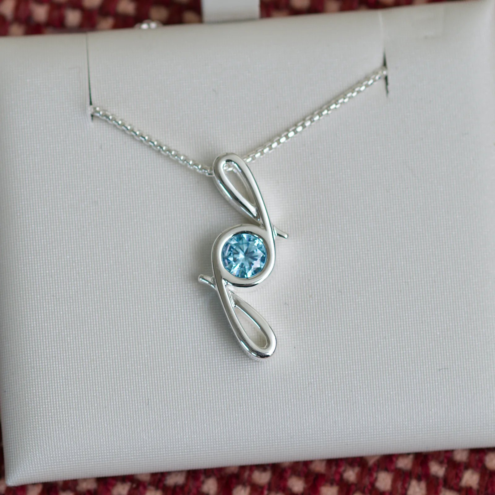 This pendant is made from tarnish resistant silver and features a simulated aquamarine birth stone. It hangs from a 1mm rounded box chain. The design is a signature motif that symbolizes our message that every life is a precious life.