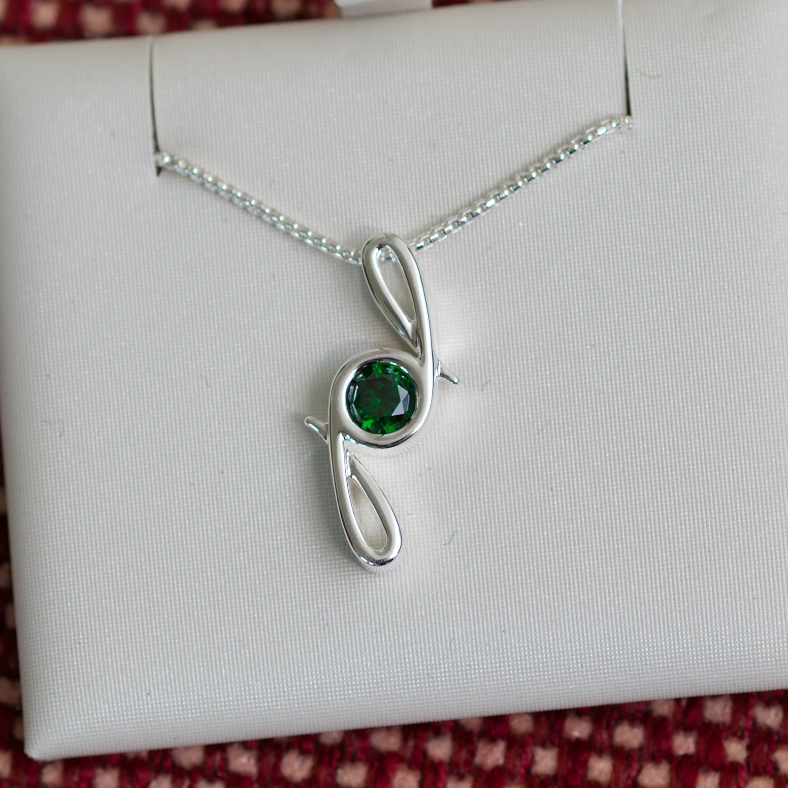 This pendant is made from tarnish resistant silver and features a simulated emerald birth stone. It hangs from a 1mm rounded box chain. The design is a signature motif that symbolizes our message that every life is a precious life.
