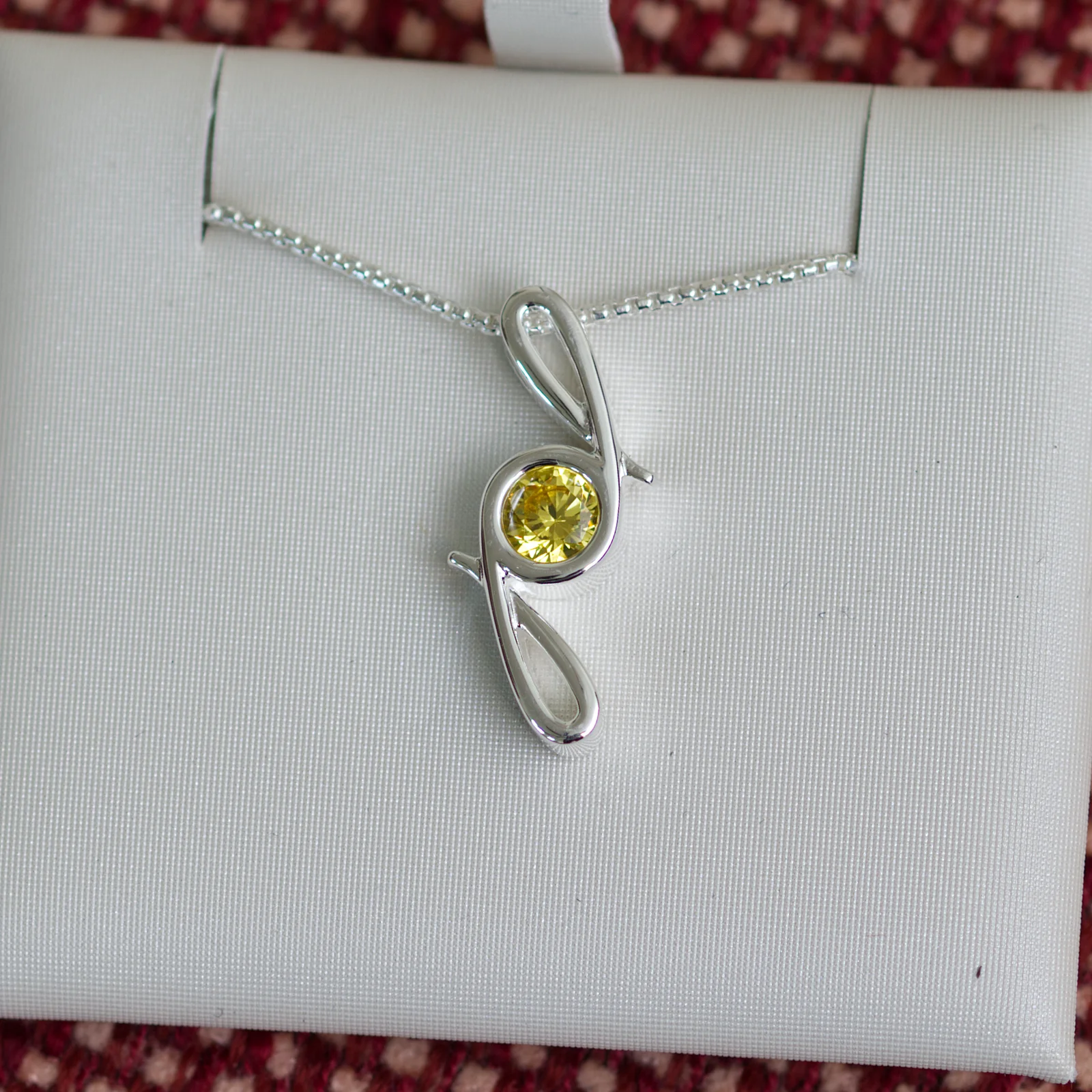 This pendant is made from tarnish resistant silver and features a simulated citrine birth stone. It hangs from a 1mm rounded box chain. The design is a signature motif that symbolizes our message that every life is a precious life.