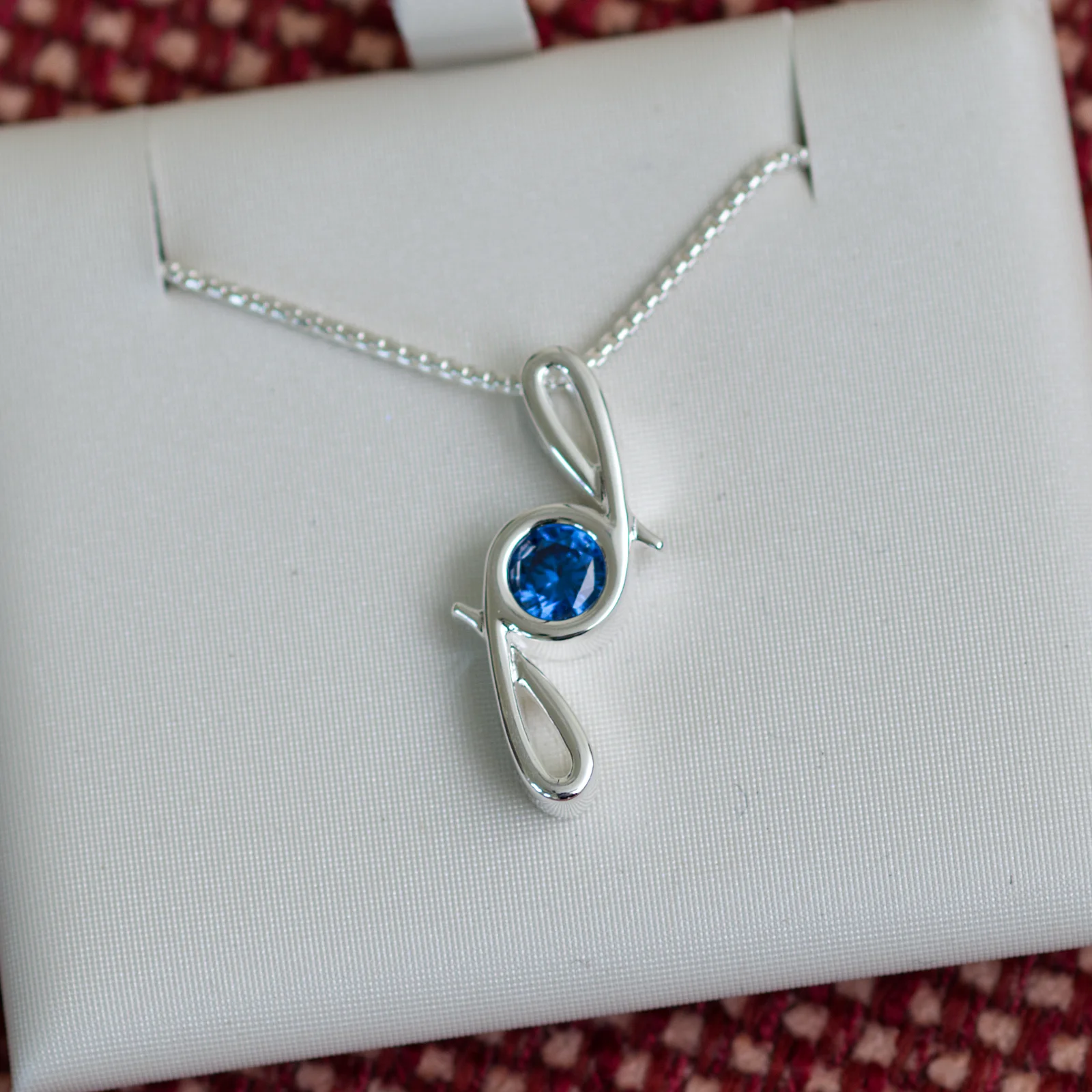 This pendant is made from tarnish resistant silver and features a simulated sapphire birth stone. It hangs from a 1mm rounded box chain. The design is a signature motif that symbolizes our message that every life is a precious life.